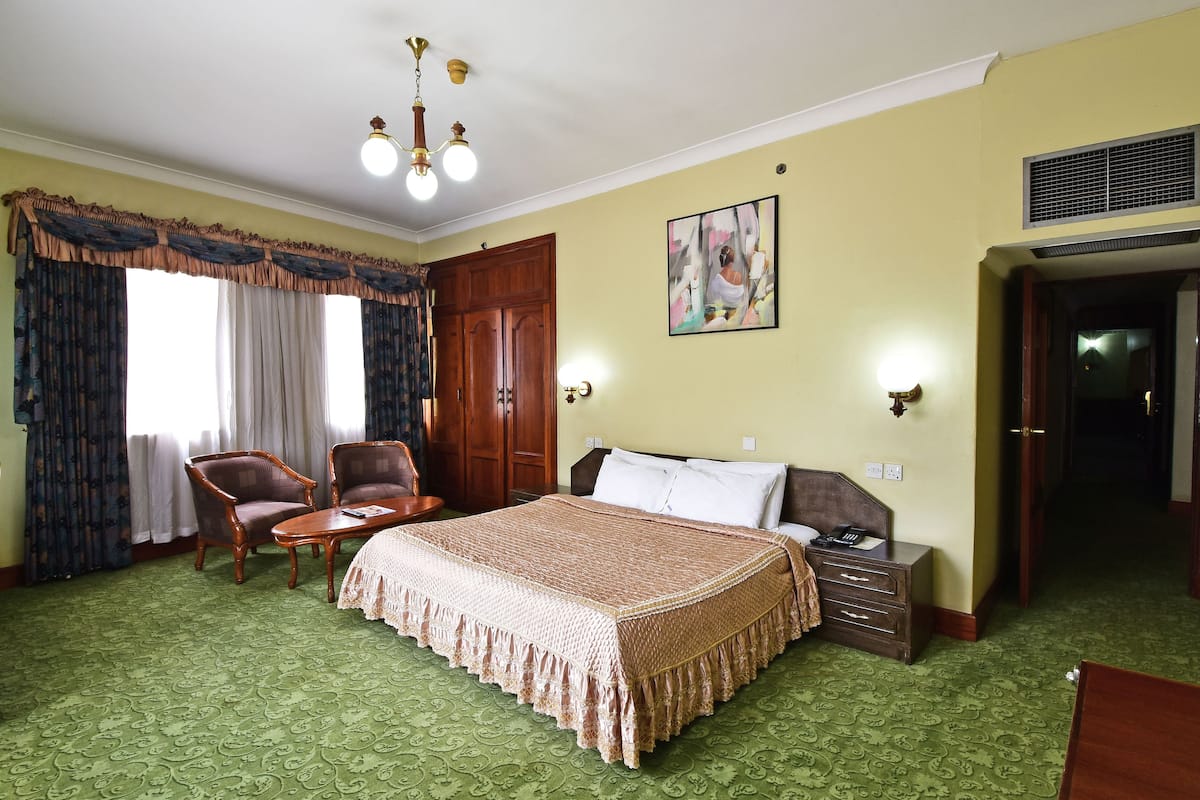 A hotel room with a large bed, two armchairs, a small table, a nightstand, and a painting on the wall.