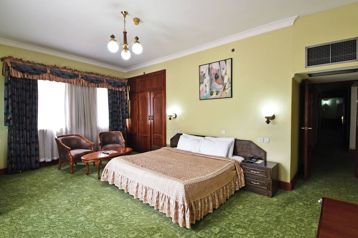 A hotel room with a large bed, two armchairs, a small table, and a nightstand.