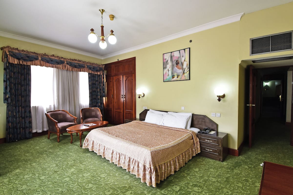 A hotel room with a large bed, two armchairs, a small table, a nightstand, and a painting on the wall.