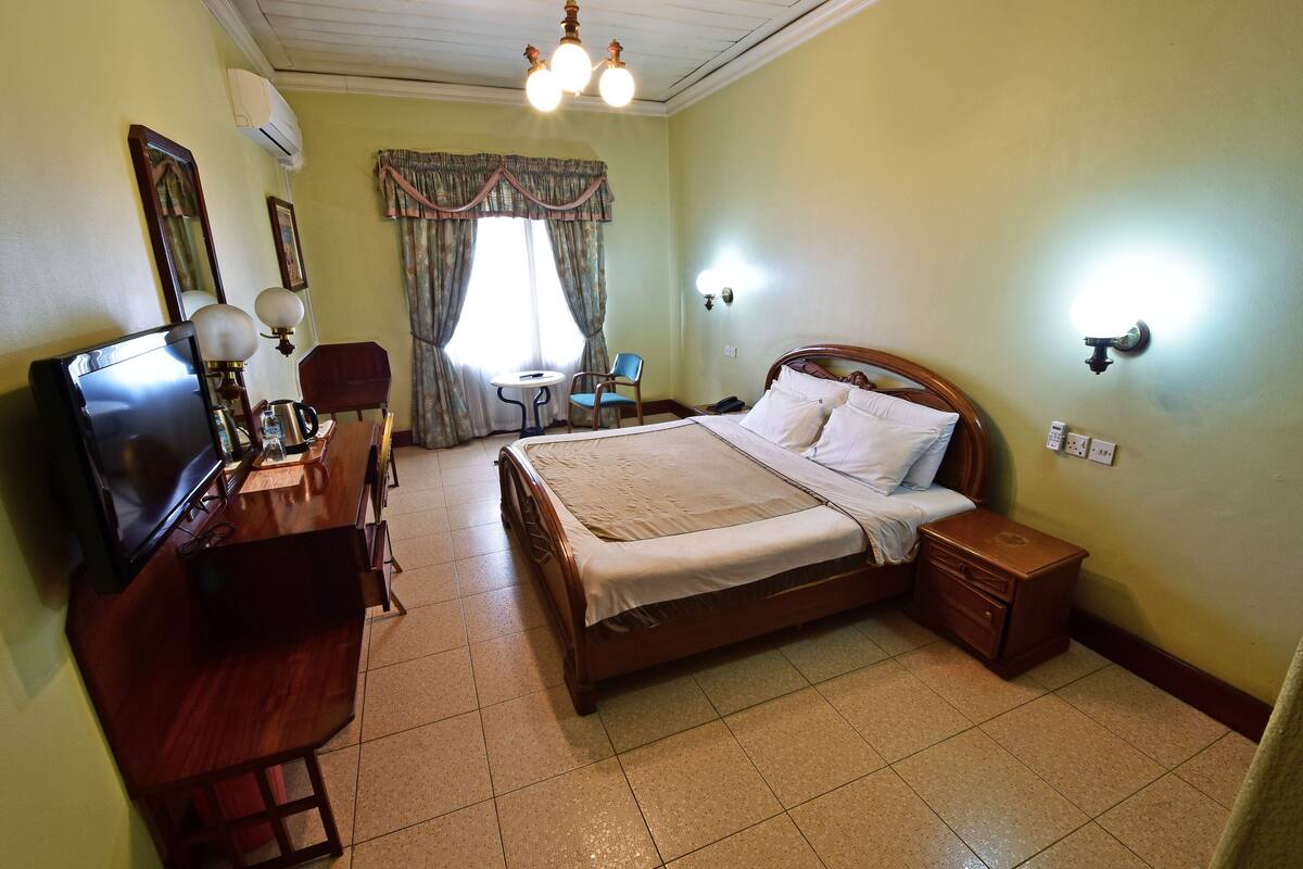 A hotel room with a wooden bed, a desk with a television, a chair, and a small table.