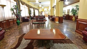 A spacious lobby with a large wooden table in the center, surrounded by leather sofas and chairs. - Grand Imperial Hotel (Kampala)