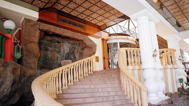 A grand staircase with a wooden handrail leading to a lobby area with a sign reading "Grand Imperial Hotel". - Grand Imperial Hotel (Kampala)