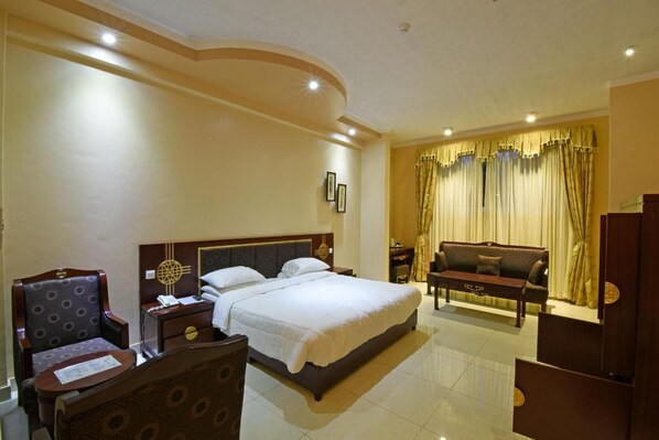A hotel room with a large bed, a sofa, a chair, a nightstand, and a desk. - Imperial Resort Beach Hotel (Entebbe)