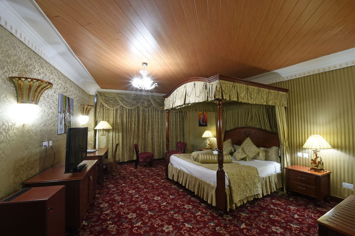 A four-poster bed with a canopy, a television on a desk, and lamps on nightstands.