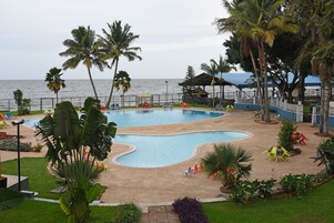Un área de piscina con varias piscinas, palmeras y vista al océano.