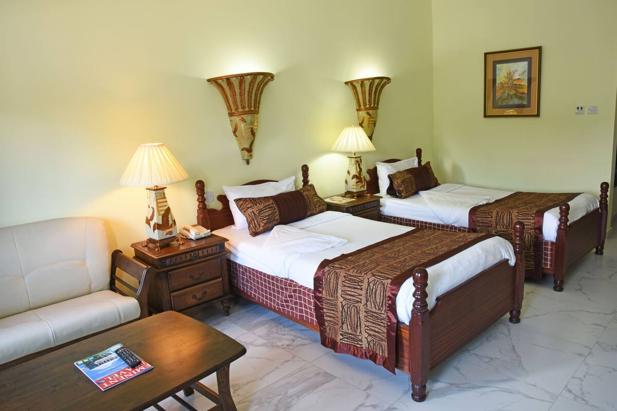 A hotel room with two beds, a sofa, a table, and two wall-mounted lamps.
