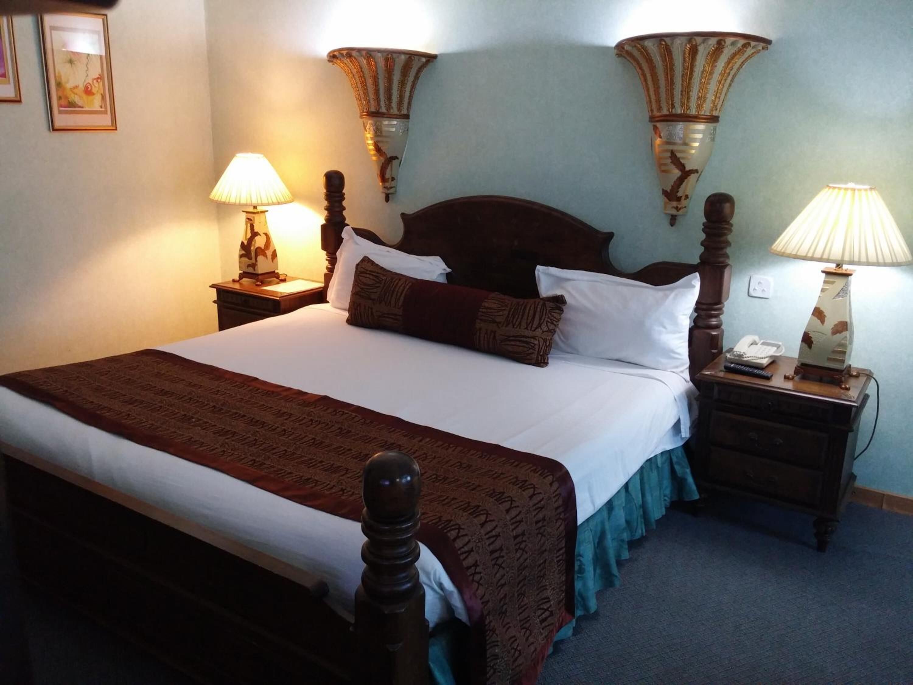 A neatly made bed with a wooden headboard, two bedside lamps, and a telephone on a wooden nightstand.
