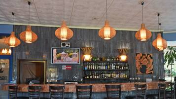 Angolo bar con bancone in marmo, diverse lampade a sospensione arancioni, televisore a parete e cartello 'Vietato fumare'.