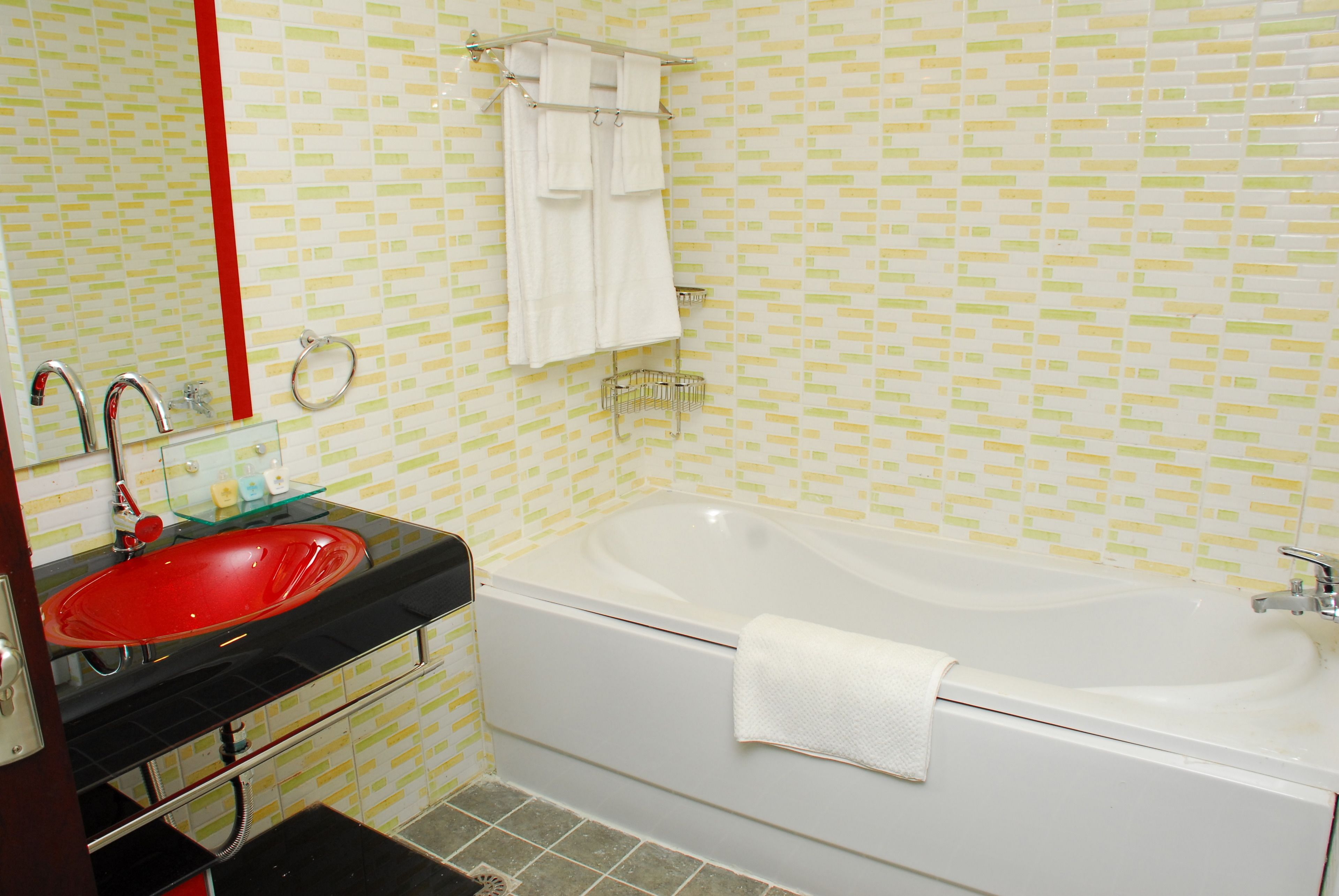 A bathroom with a red sink, white bathtub, and a mirror above the sink.