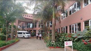 A building with a red facade, palm trees, and a white van parked in front. - Imperial Golf View Hotel (Entebbe)