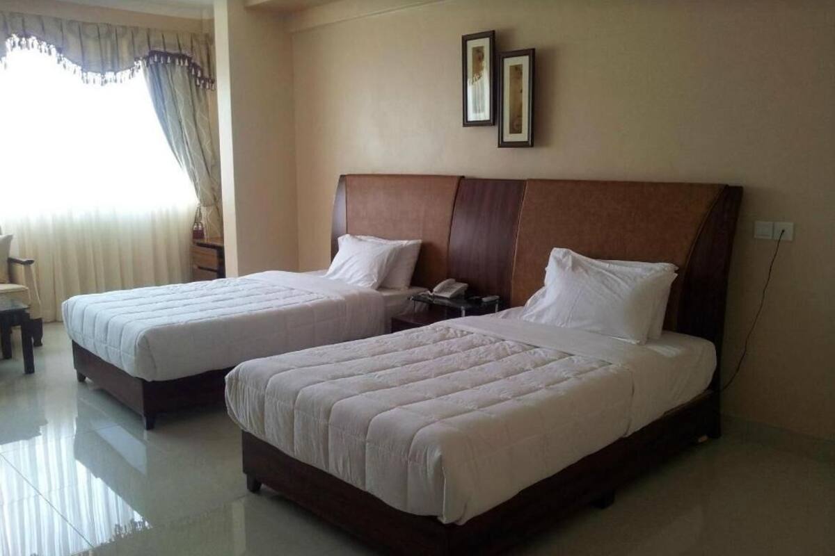 A hotel room with two beds, a nightstand, a chair, and a window with curtains.