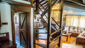 A rustic interior with a wooden staircase, a stone wall, and a cozy living area with a sofa and a coffee table. - Oikoperiigitis Hotel (Sintiki)