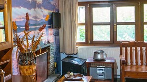 A cozy room with a fireplace, wooden furniture, and a scenic mural on the wall. - Oikoperiigitis Hotel (Sintiki)
