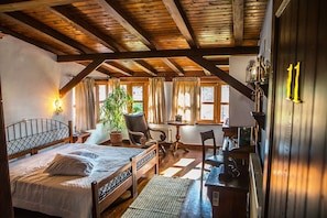 A cozy room with a wooden ceiling, a bed with a metal headboard, a chair, a table, and a potted plant. - Oikoperiigitis Hotel (Sintiki)