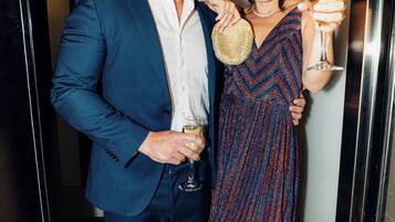 A man and a woman standing in a hallway, holding drinks.