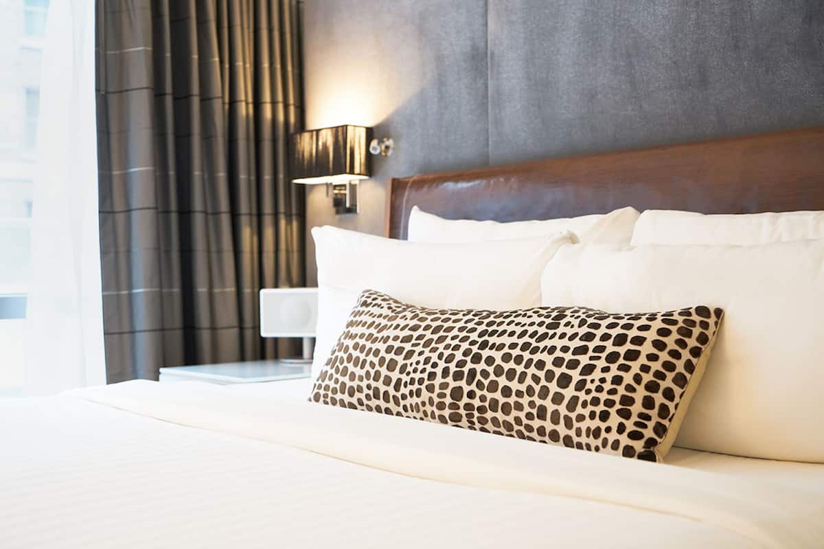 Una habitación de hotel con una cama grande, cabecera, mesita de noche y una lámpara.