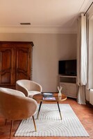 A living room with a round coffee table, two armchairs, a television on a cabinet, and a large wooden wardrobe.