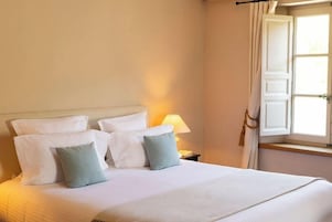 A neatly made bed with white and light blue pillows, a bedside lamp, and a window with curtains.