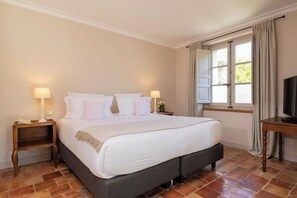 Un dormitorio con cama, dos mesitas de noche, televisor y ventana con cortinas.