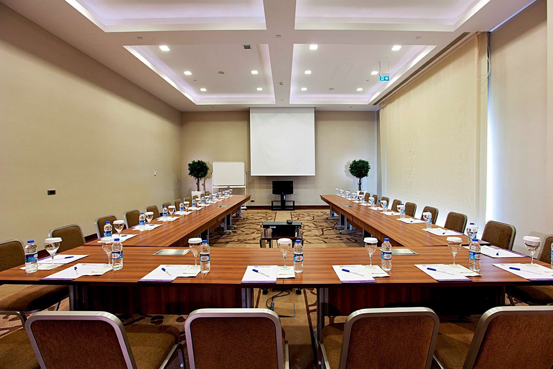 A conference room with long tables, chairs, water bottles, and a projector screen.
