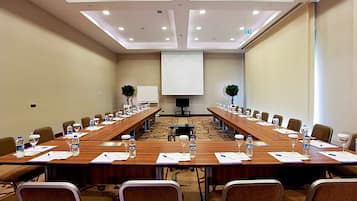 A conference room with long tables, chairs, water bottles, and a projector screen.