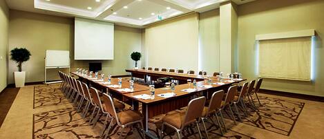 A conference room with a long table, chairs, a projector screen, and a whiteboard.