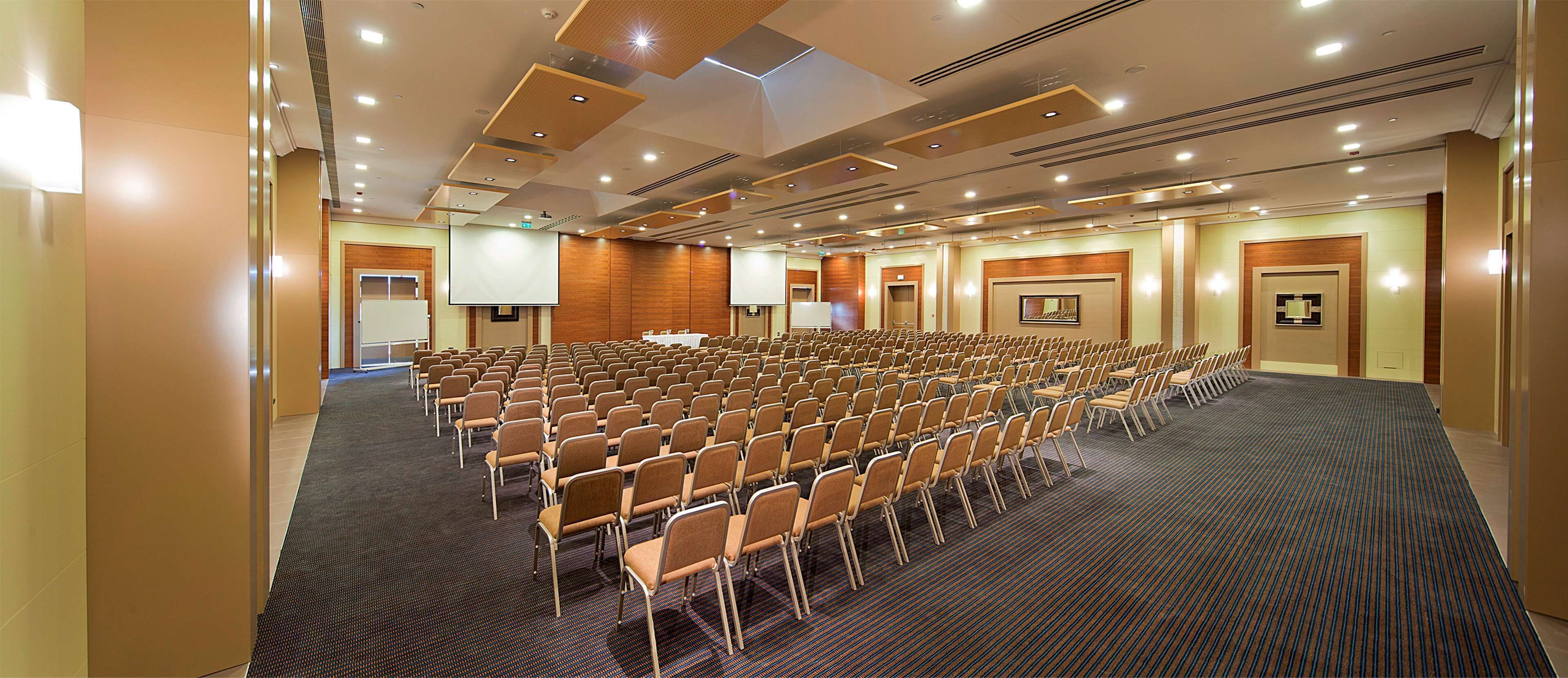 A large conference room with rows of chairs, a projector screen, and a carpeted floor.