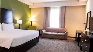A hotel room with a bed, a sofa, a TV, a lamp, and a window with curtains.