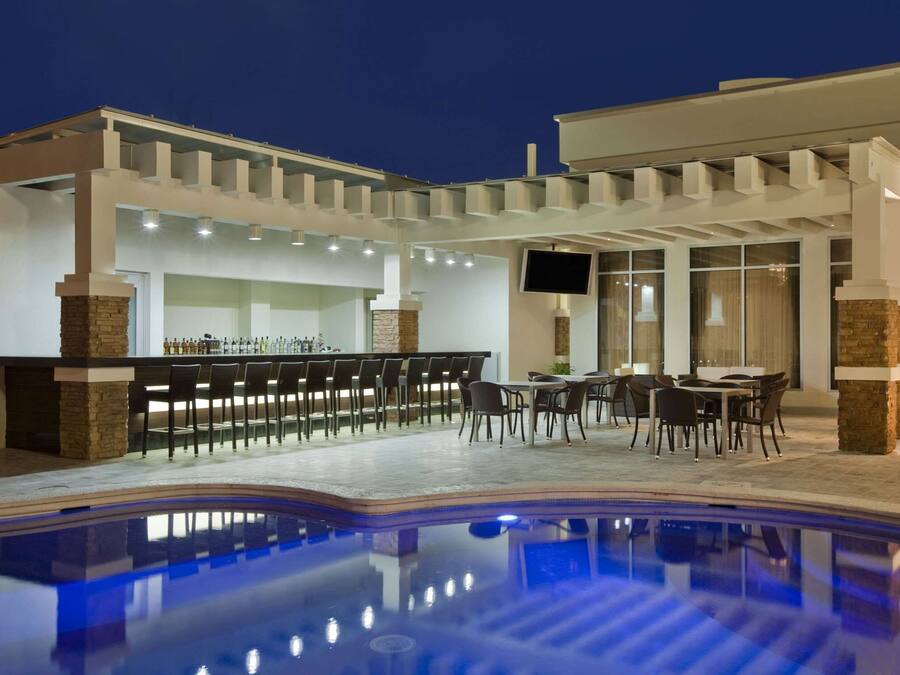 An outdoor bar area with a pool, bar stools, and tables.