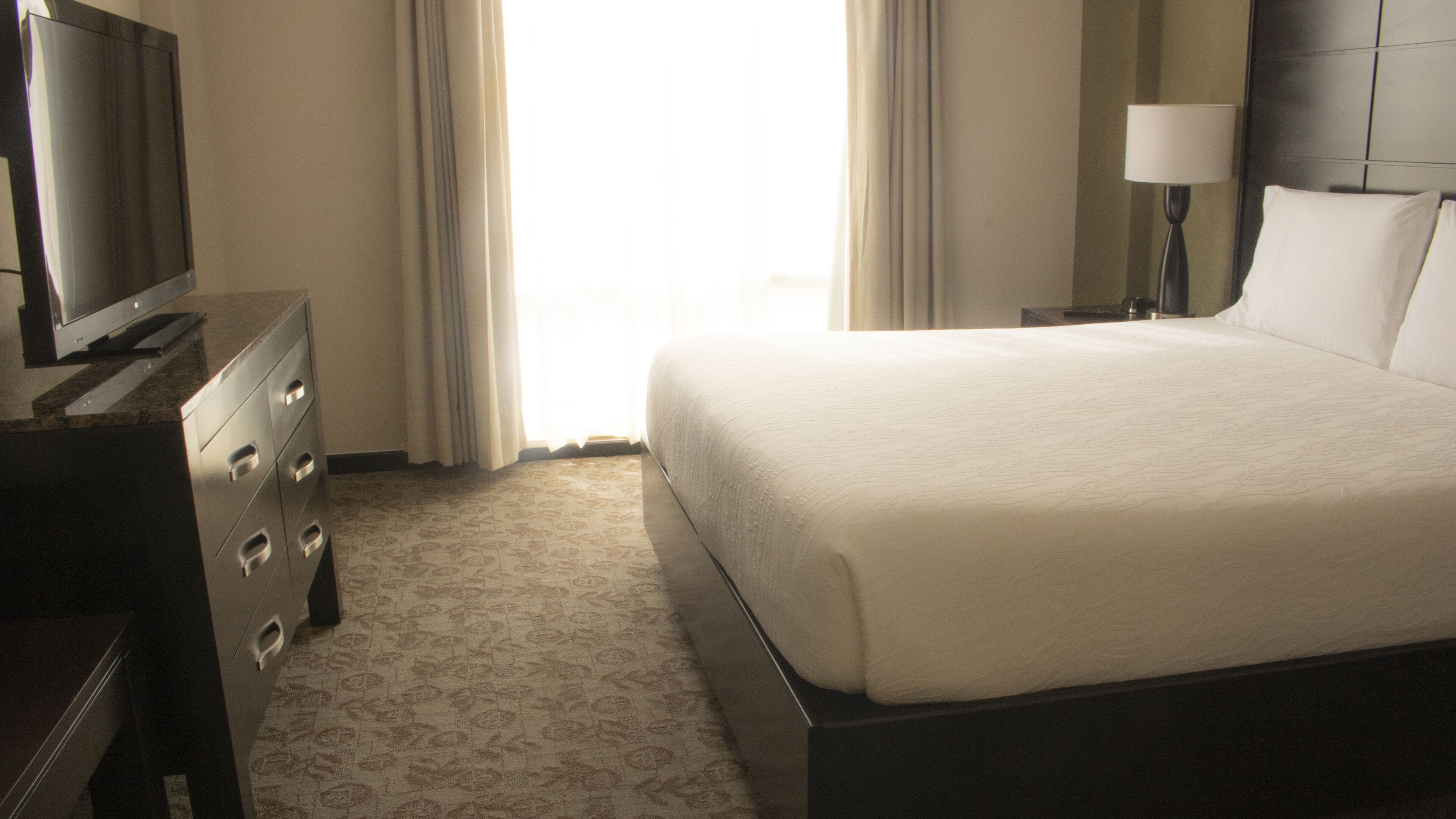 A hotel room with a bed, a dresser, a television, and a lamp.