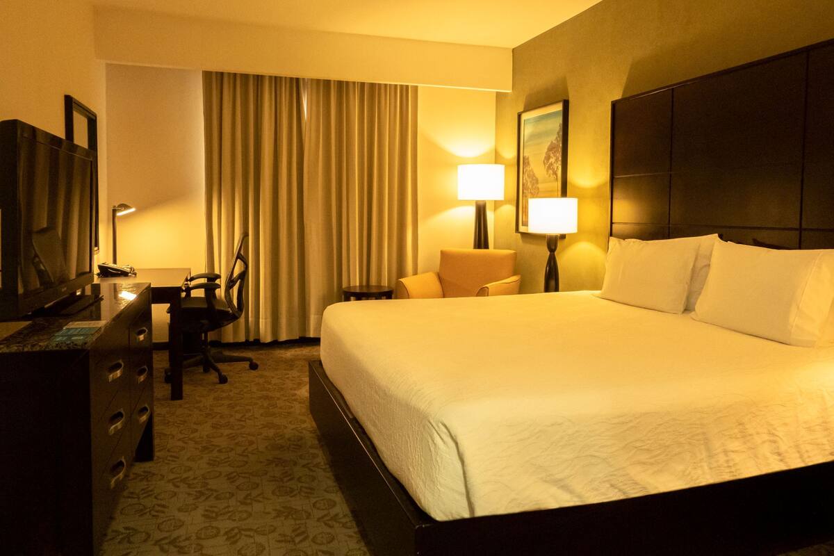 A hotel room with a large bed, a desk with a chair, a television, and a lamp.