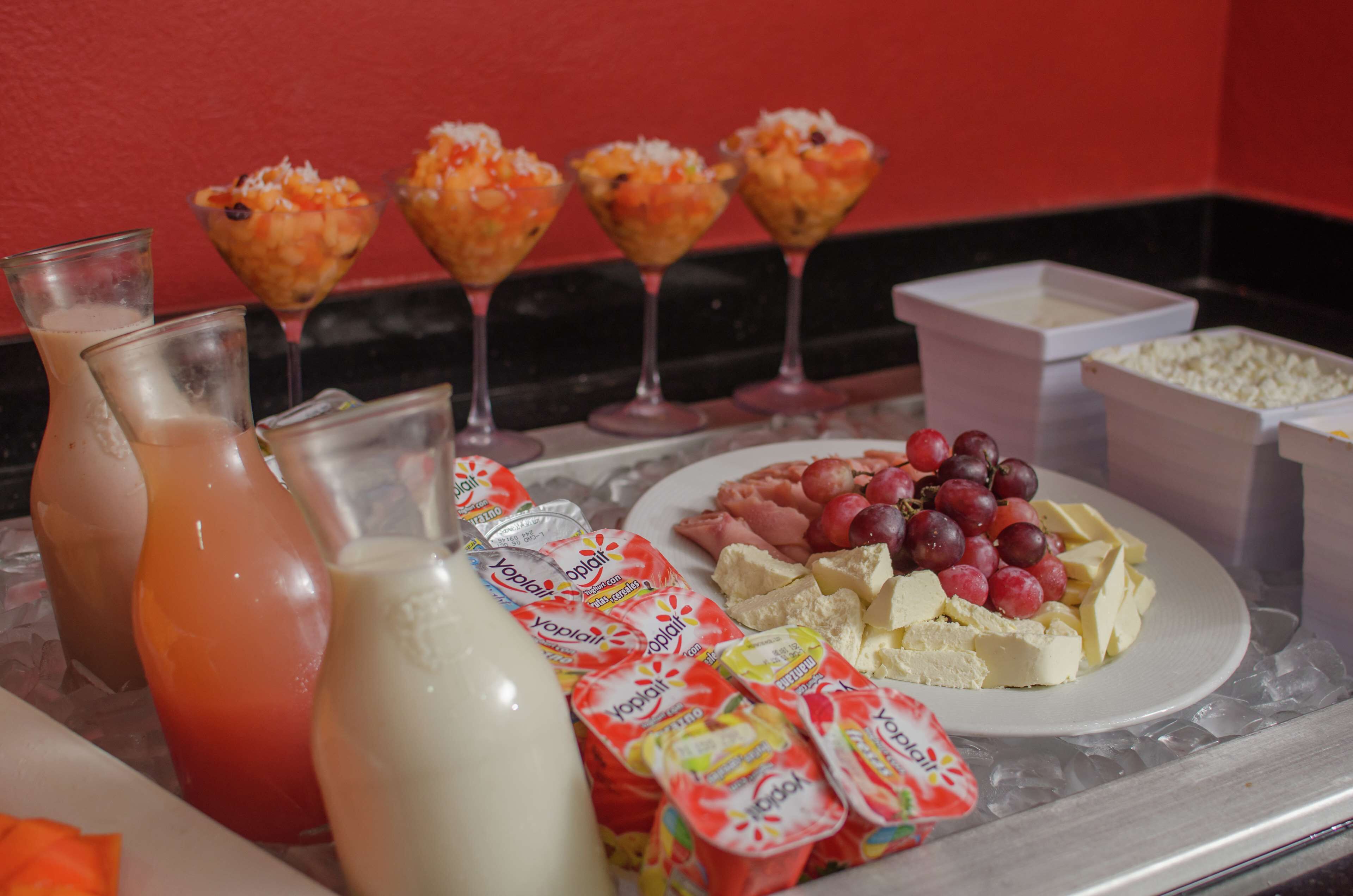 Una bandeja con diversos alimentos, incluyendo yogur, queso, uvas y una bebida.