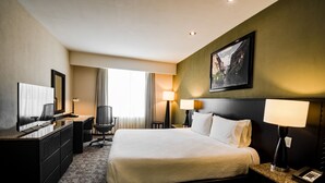 Una camera d'albergo con un letto grande, una scrivania con un computer, una sedia, una lampada e un quadro appeso al muro.