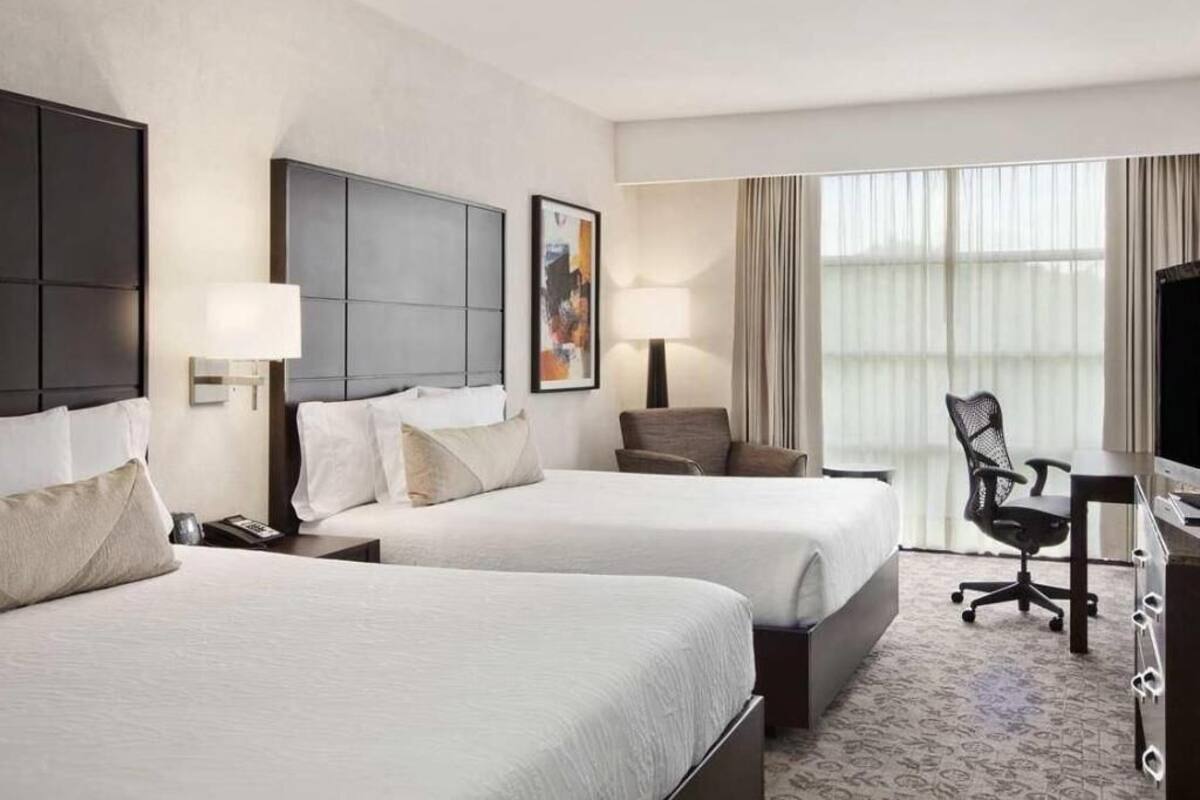 A hotel room with two beds, a desk, a chair, and a television.