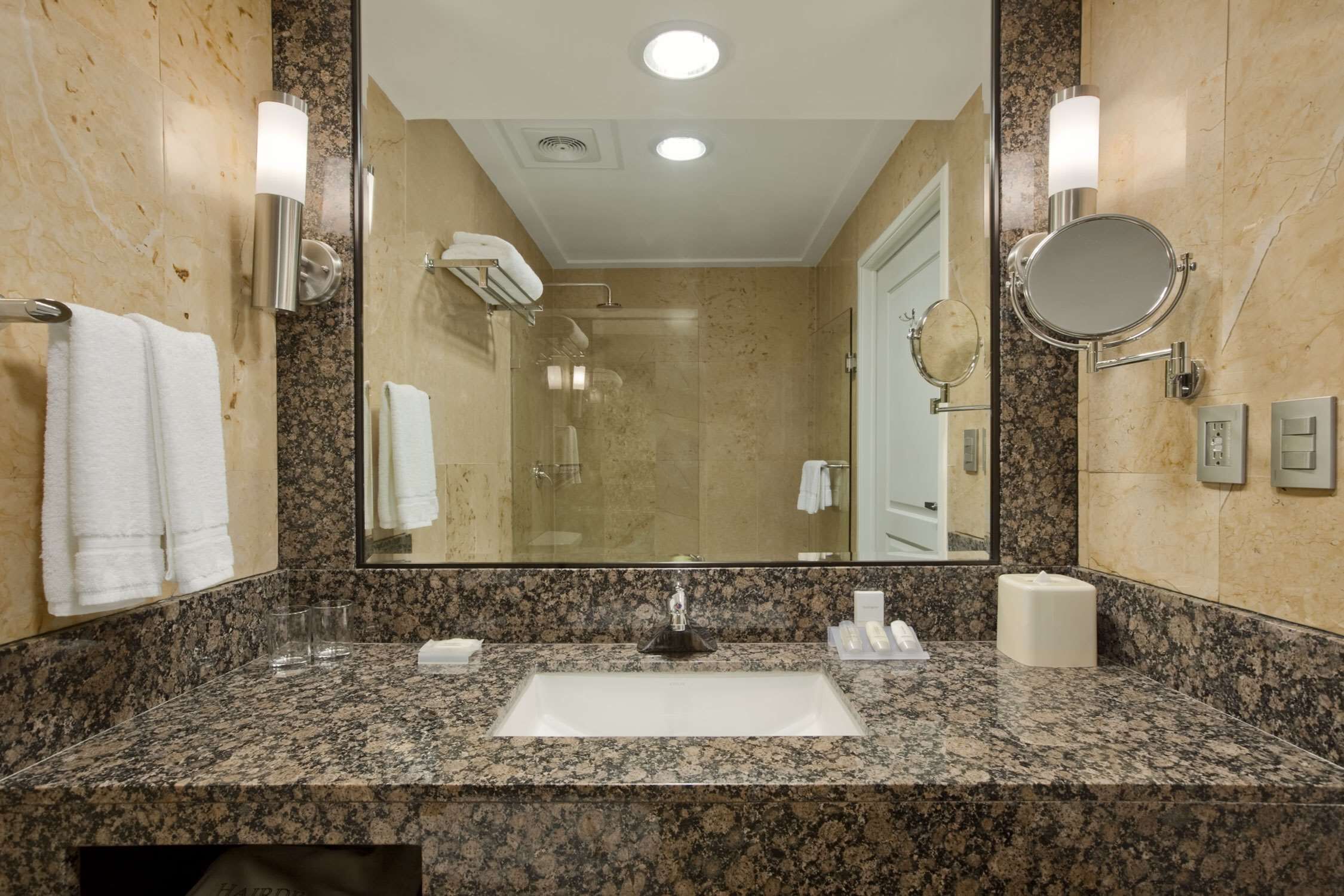 A bathroom with a granite countertop, a white sink, a mirror, and two wall-mounted light fixtures.