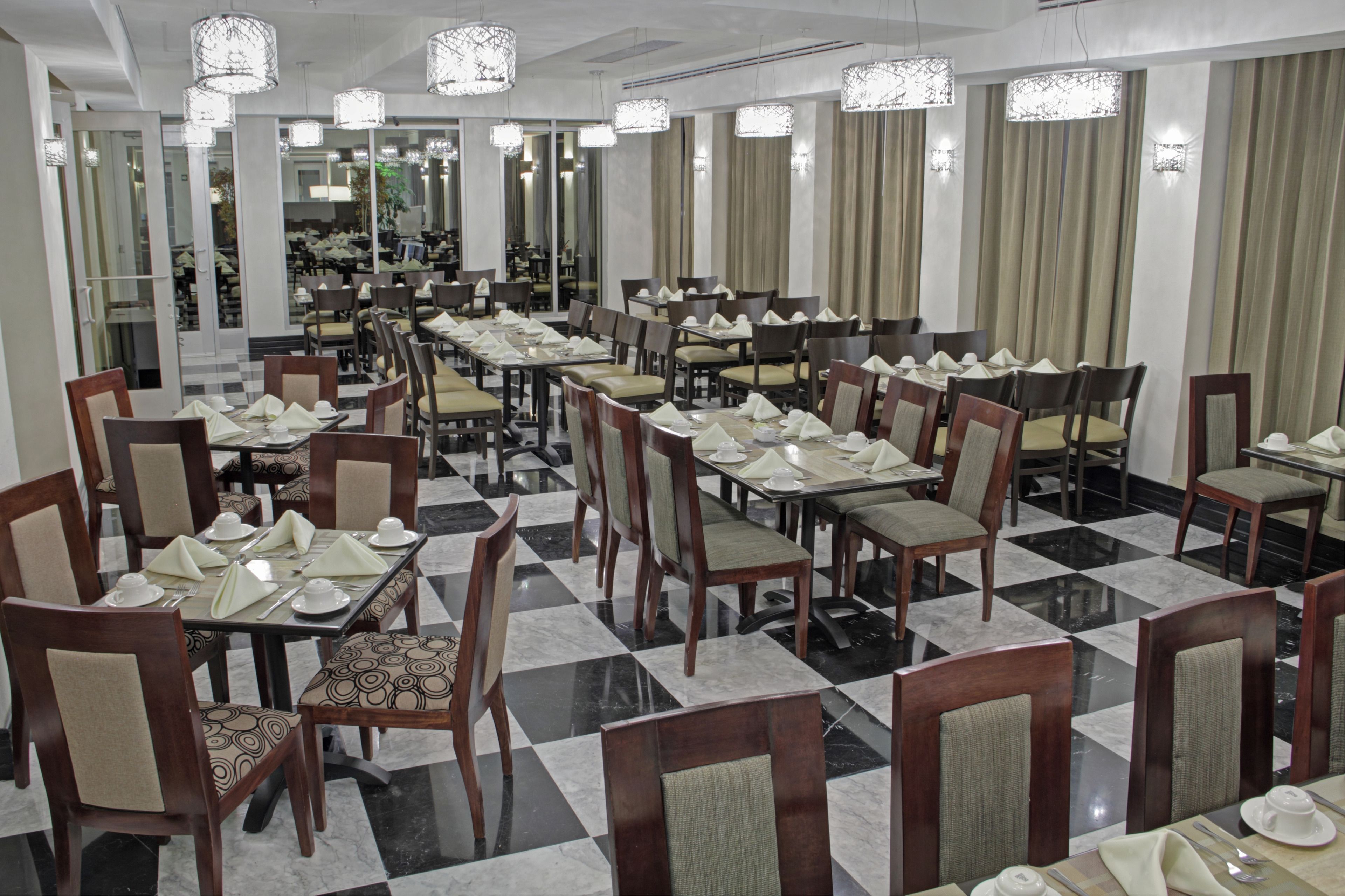 A hotel dining area with multiple tables set for service, chairs, and chandeliers.