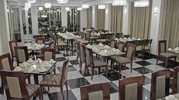 Een restaurant in een hotel met meerdere gedekte tafels, stoelen en kroonluchters.