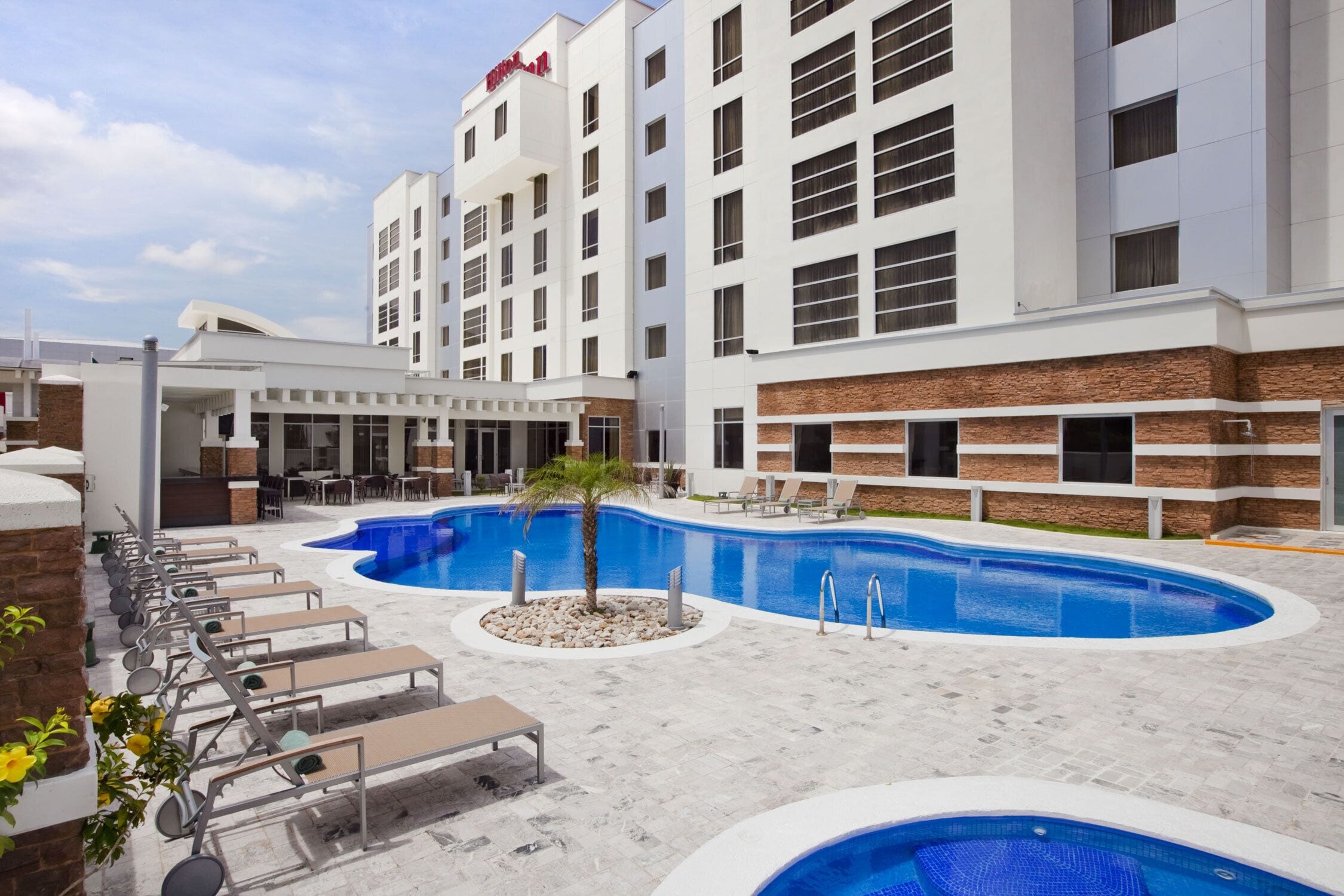 A hotel with a large outdoor swimming pool, lounge chairs, and a brick facade.