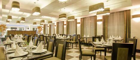 A hotel dining area with multiple tables set for service, chandeliers, and a checkered floor pattern.