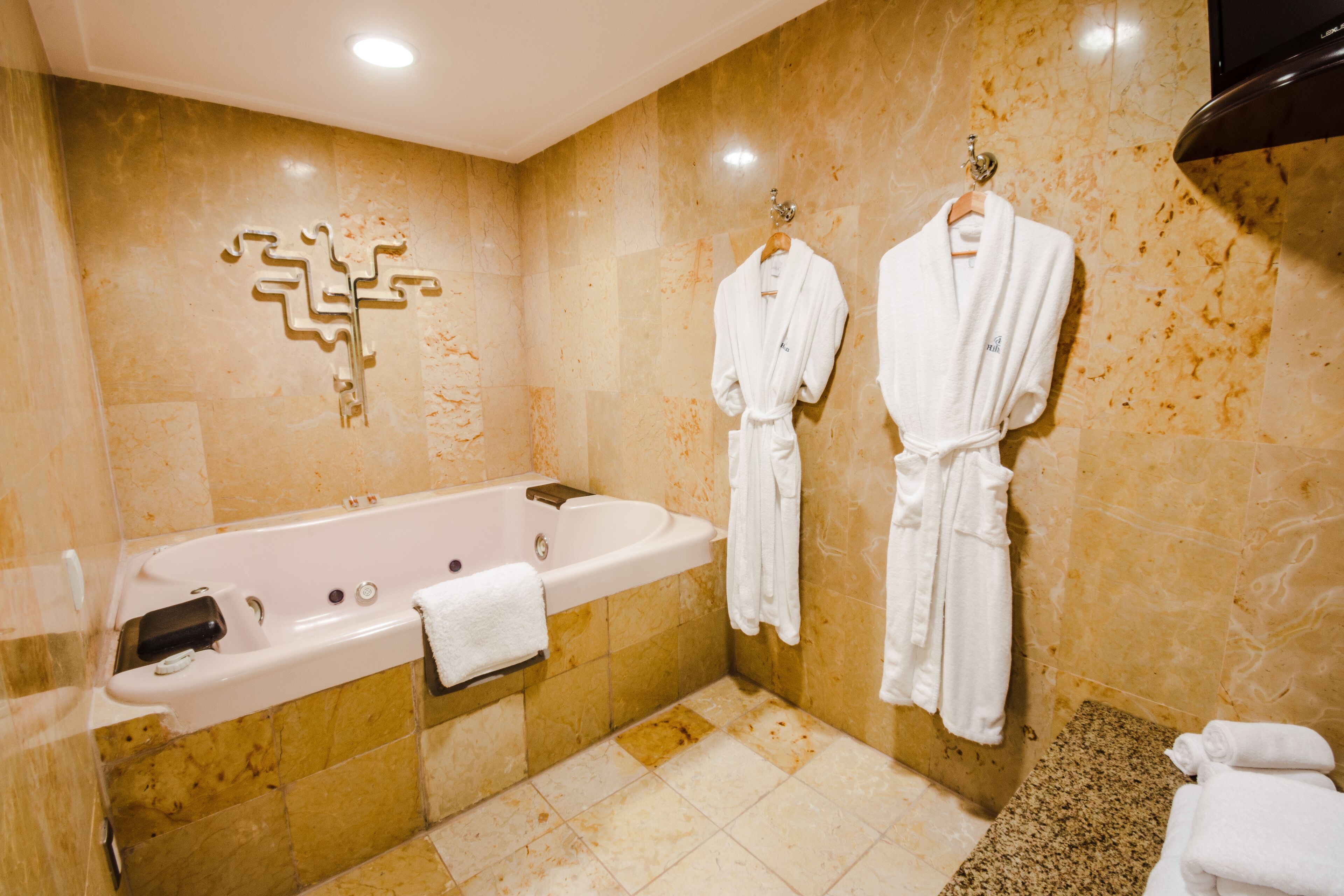 Un baño con una bañera grande, dos batas blancas colgadas en ganchos y una pared de mármol.