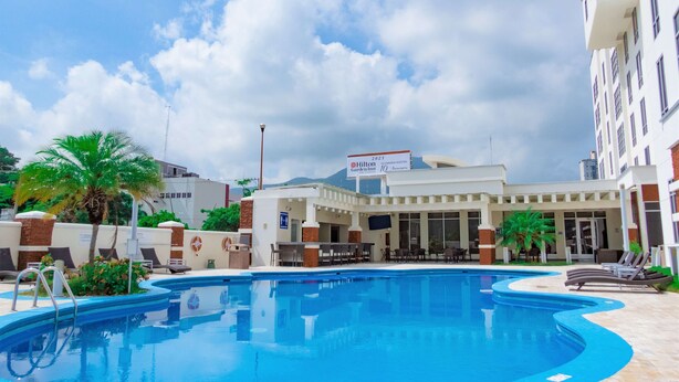 Area piscina con lettini, una palma e un edificio con un cartello che indica un Hilton Garden Inn.