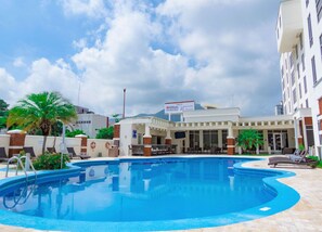 A swimming pool area with lounge chairs, a palm tree, and a building with a sign indicating a Hilton Garden Inn. - Hilton Garden Inn Tuxtla Gutierrez (Tuxtla Gutierrez)