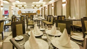 Un'ampia sala da pranzo con numerosi tavoli apparecchiati per il servizio, caratterizzata da un pavimento a scacchi e moderne lampade.