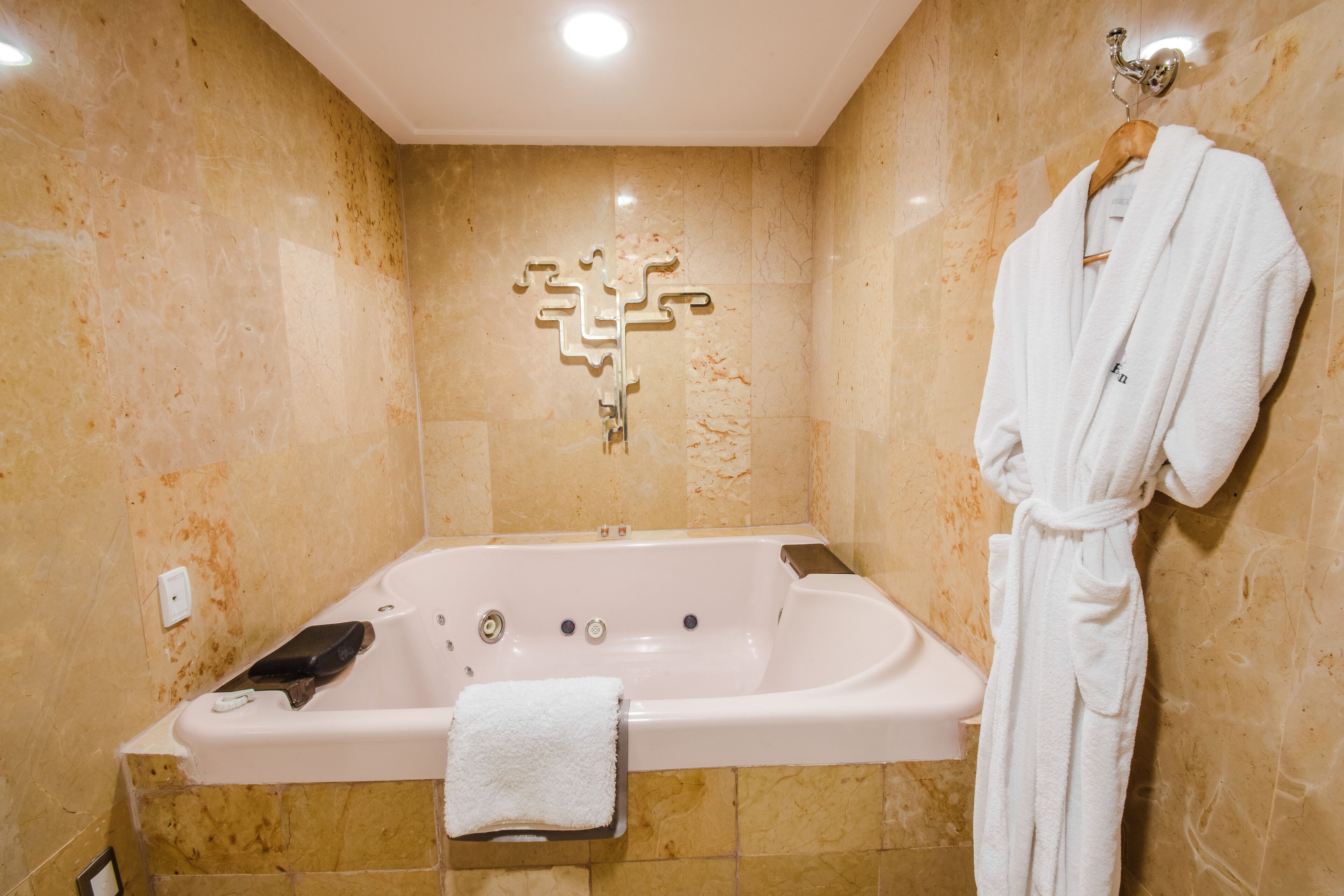 A bathroom with a large bathtub, a towel, and a robe hanging on a hook.
