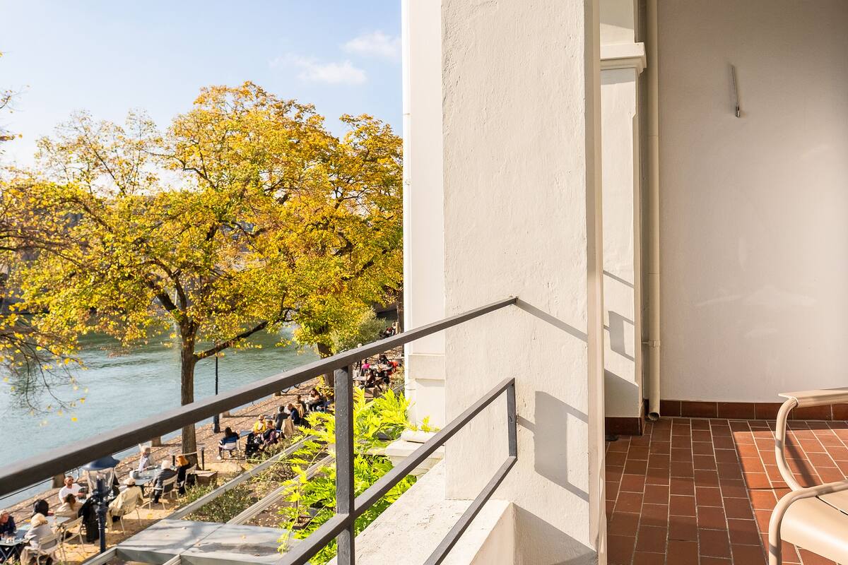 A balcony with a view of a river and trees, a tiled floor, and a railing.