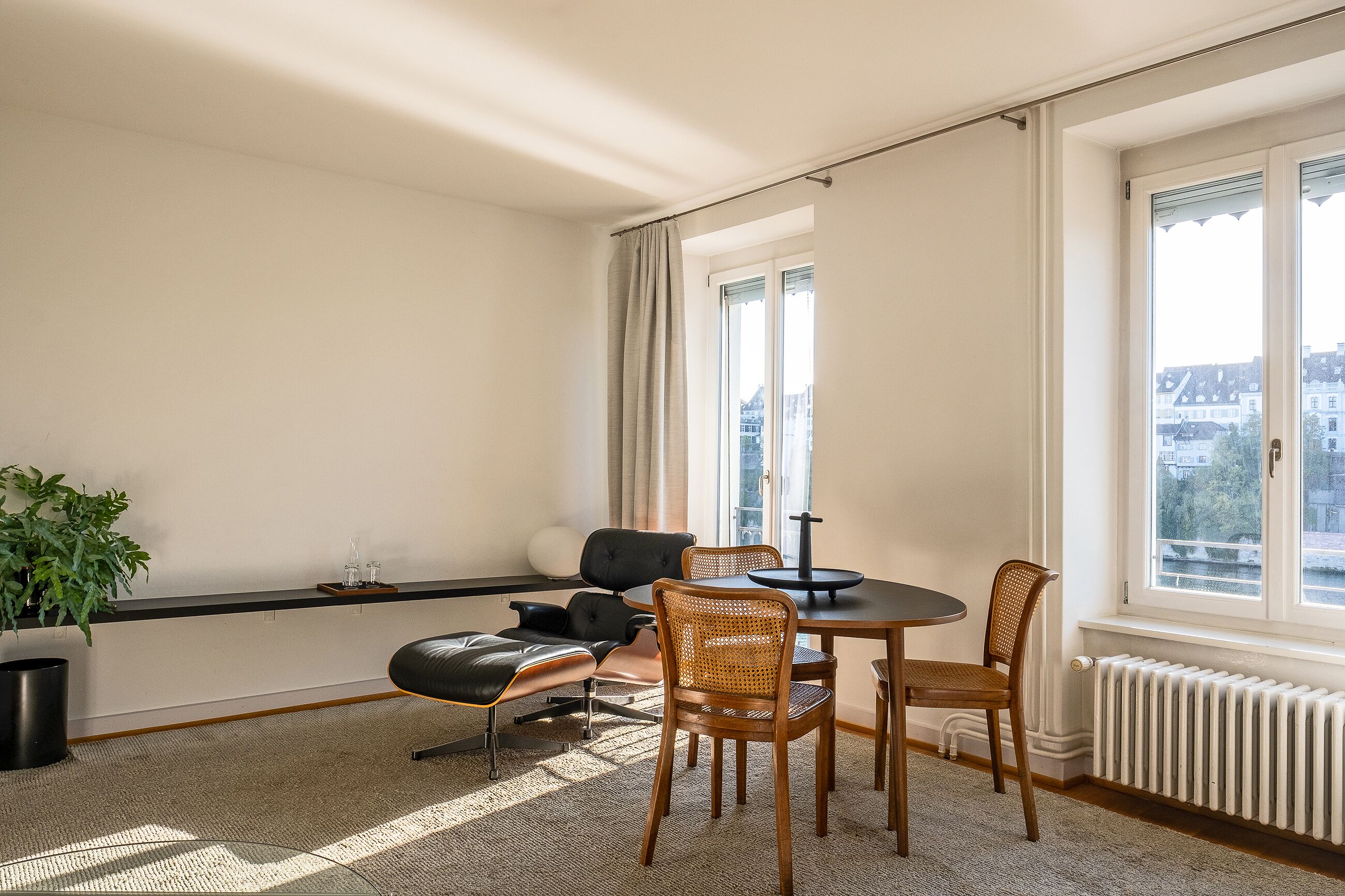 Ein modernes Zimmer mit Esstisch, Stühlen, einer Topfpflanze und einem Heizkörper.