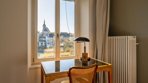 A room with a view of a church through a window, a table with a lamp, and a radiator. - Krafft Basel (Basel)