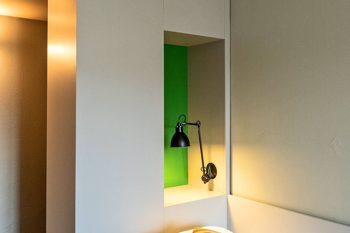 A modern hotel room with a bed, a bedside lamp, and a green accent wall.