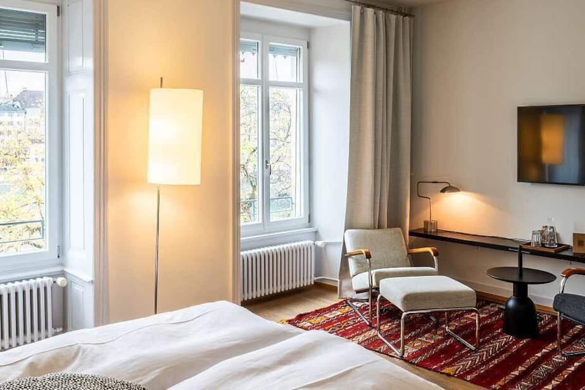 A hotel room with a bed, a desk, a chair, a TV, and a window with curtains.