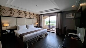 A hotel room with a large bed, two bedside lamps, a flat-screen TV, and a balcony with a view. - Hotel Del Rio (Iloilo)